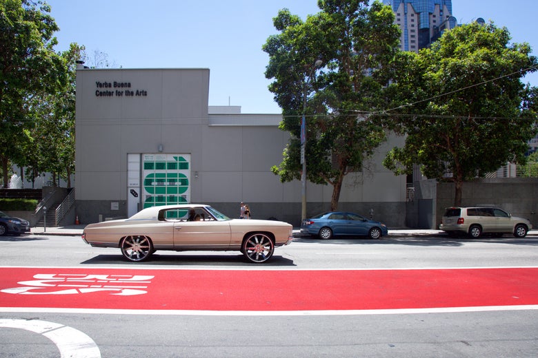 A white car and a red bus lane on a San Francisco street.
